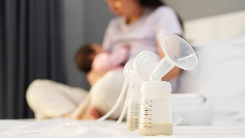 pumped breastmilk and mother breastfeeding baby in the background