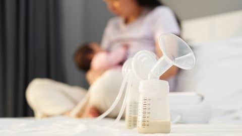 pumped breastmilk and mother breastfeeding baby in the background