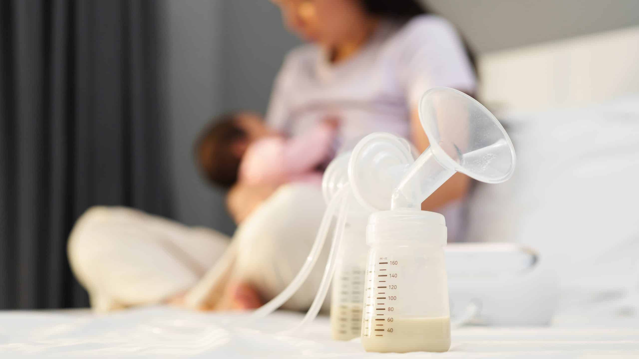 pumped breastmilk and mother breastfeeding baby in the background