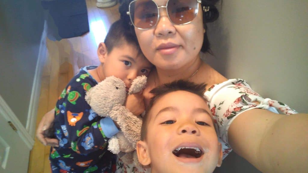 Milk donor Bicky takes a selfie while holding one child close, with another smiling playfully in front of the camera.