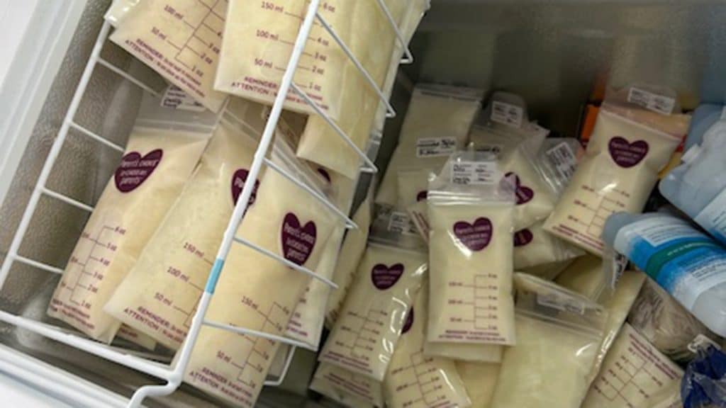 Dozens of labeled donor milk bags, some marked with heart stickers, are neatly stacked inside a freezer drawer.