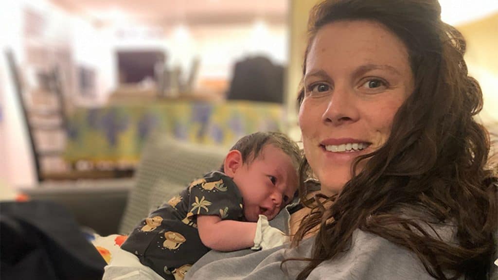 Milk donor Whitney holds her newborn against her shoulder, smiling softly while the baby rests peacefully in her arms.